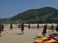People standing in circle holding kayak paddles on sandy beach with kayaks on the ground 